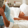 Worried Senior Woman Sits On Bed Whilst Husband Sleeps